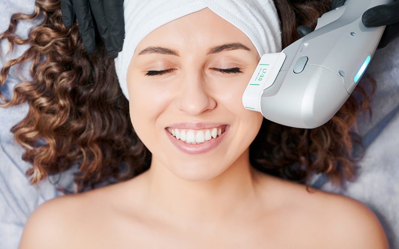 young smiling brunette woman getting aesthetics facial treatment