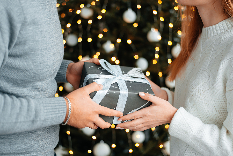 man and woman exchanging gift in front of Christmas tree